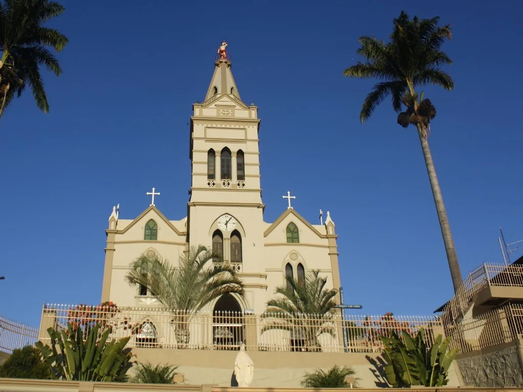 Fachada da Igreja Matriz São Sebastião de Inhapim MG, com torre, relógio e palmeiras ao lado