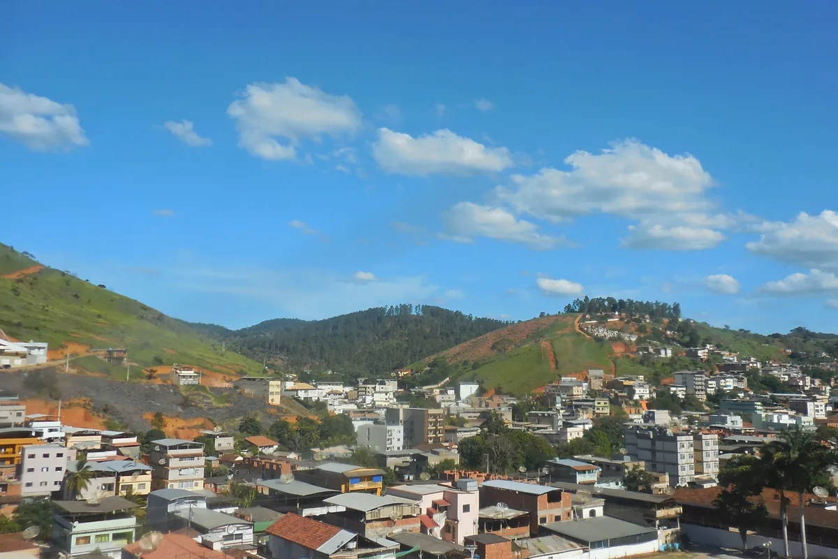Panorâmica de Inhapim MG mostrando o casario subindo as encostas e as serras ao fundo sob céu azul